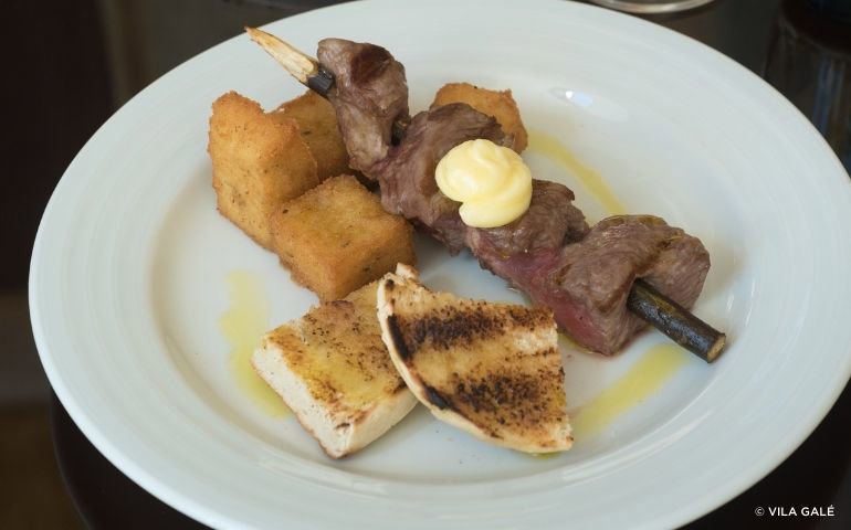 Beef skewers on a bay tree branch with fried corn cubes